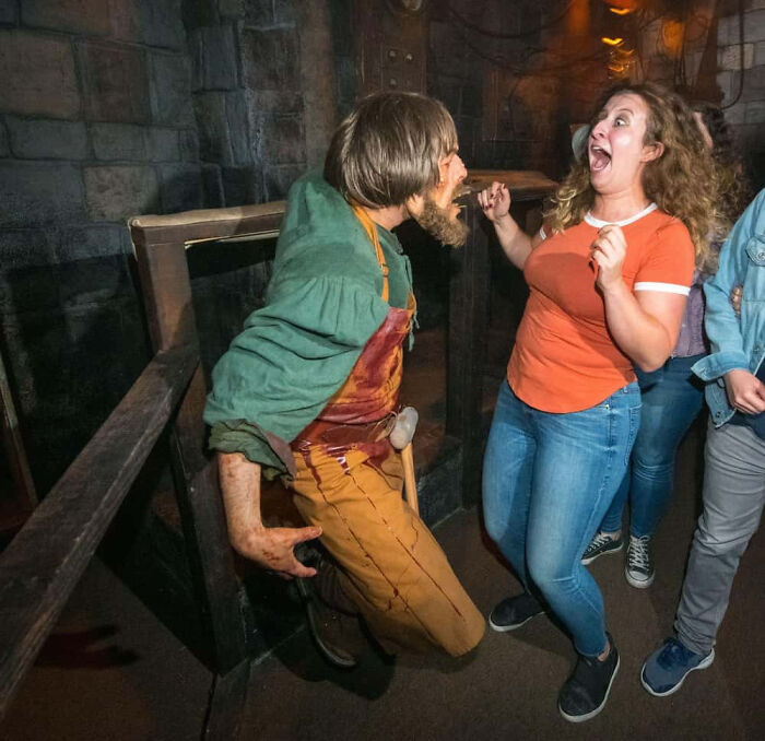 A terrified woman screams in shock as an actor in a bloody apron approaches her in a haunted house.