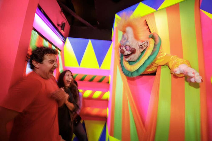 Scared man and woman reacting to a creepy clown inside a haunted house.