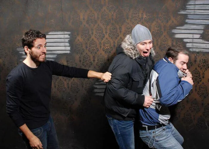 Group of men startled and holding onto each other in a haunted house photo.