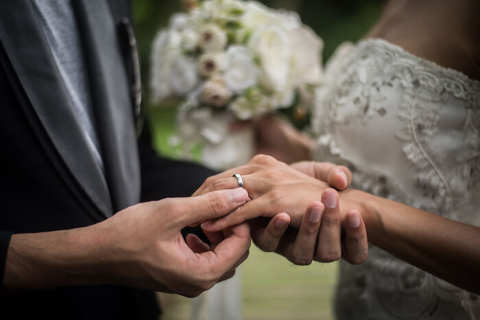 A close-up of a groom placing a ring on the bride's finger, showcasing moments leading to being disowned.