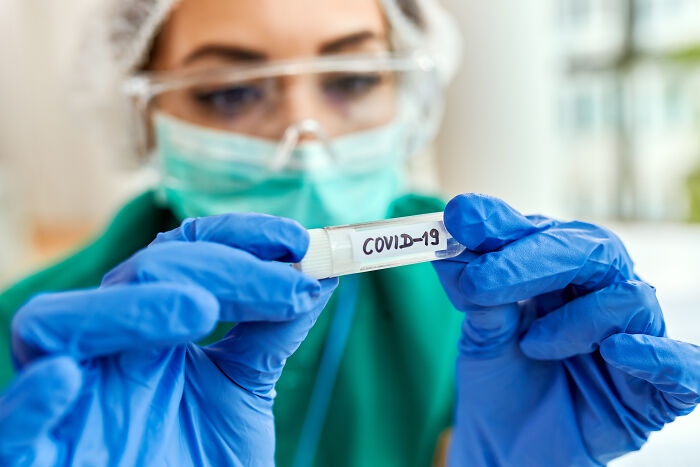 Scientist holding a vial labeled COVID-19, representing health problems now seen in Gen Z.