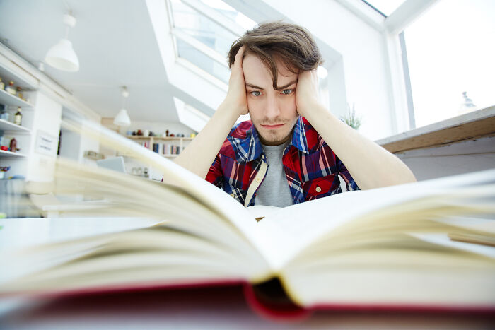 Frustrated young man with his head in his hands studying a book, illustrating health problems in Gen Z.