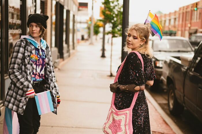 Two stylish students walking outside holding pride flags, showing the diversity among modern students.