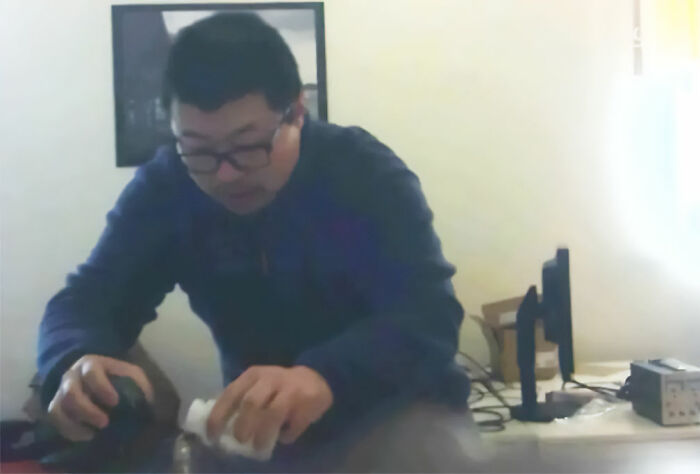 Footage from a hidden spy camera at work showing a man handling a container near a desk. Footage from a hidden spy camera at work showing a man handling a container near a desk.