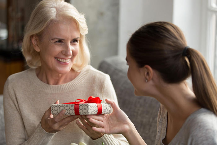 Daughter-in-law giving a wrapped gift to an older woman during family gathering Daughter-in-law giving a wrapped gift to an older woman during family gathering