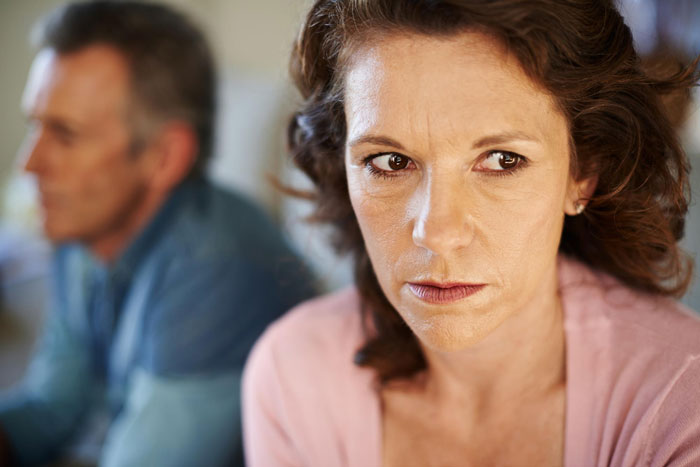 Woman looking upset with man blurred in background, depicting family tension with toxic mom Woman looking upset with man blurred in background, depicting family tension with toxic mom