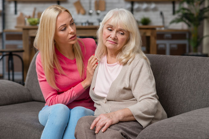 Daughter-in-law consoling upset older woman on couch family tension Daughter-in-law consoling upset older woman on couch family tension