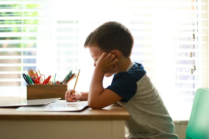 Frustrated young student writing with a pencil, feeling the pressure from infuriating teachers.