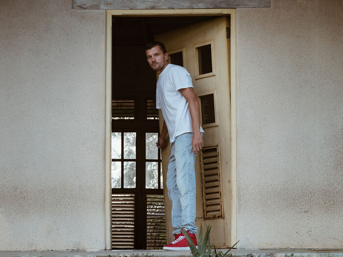 A man standing nervously at an open doorway in a spooky abandoned building