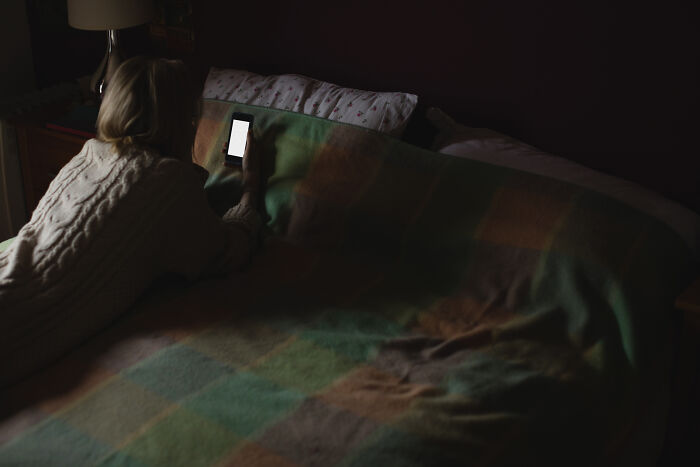 Person lying in bed looking at a smartphone screen in a dim room with spooky vibes