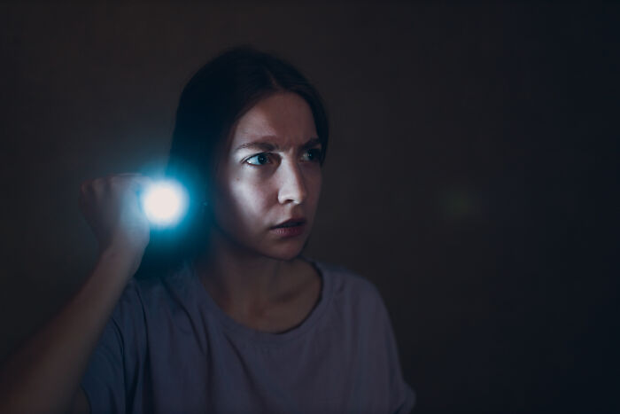 A frightened woman shining a flashlight in the dark, depicting spooky things people experienced.
