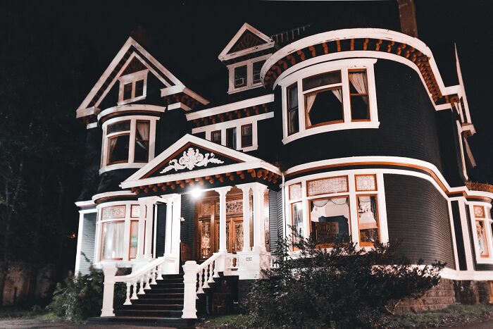 Large dark Victorian house illuminated at night, looking like one of those spooky things from real life.