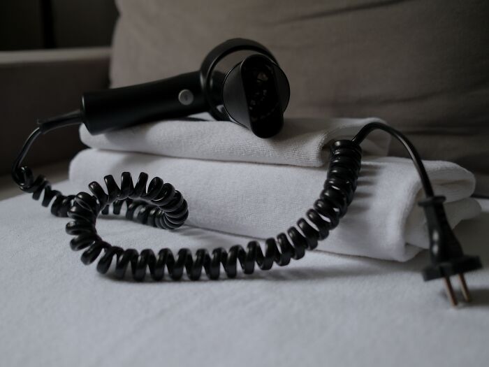 A black hair dryer on folded towels creates spooky things vibes with its eerie coiled wire.