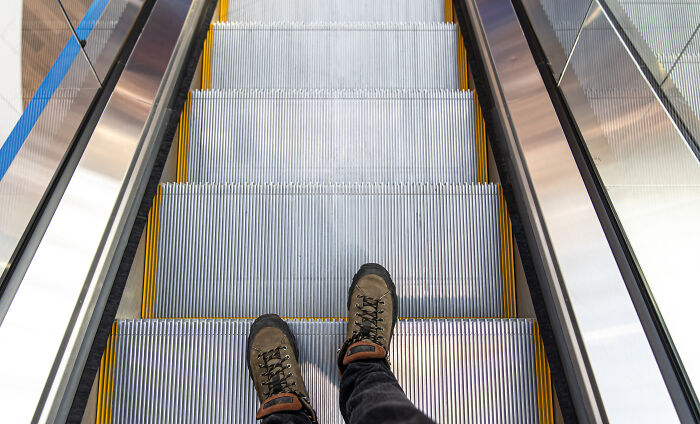 First-person view of boots standing on a descending escalator step, illustrating spooky things people experienced