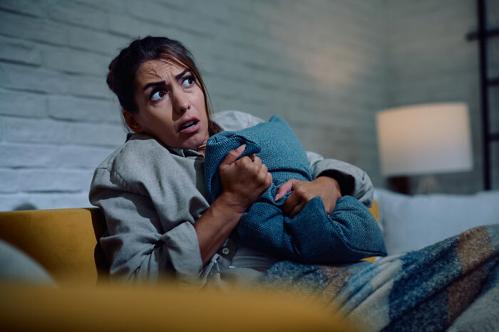 A frightened woman clutching a pillow while experiencing spooky moments at home