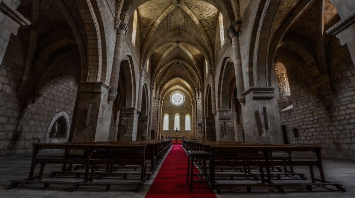 The dark interior of an ancient stone cathedral with spooky vaulted ceilings and empty pews