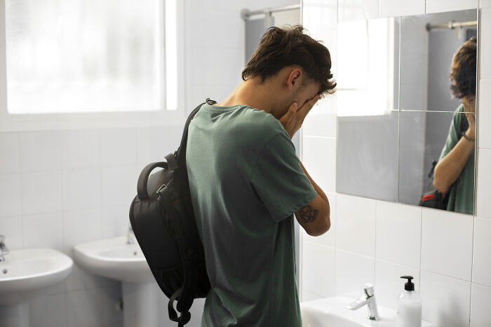 A man holding his face in his hands while looking into a bathroom mirror