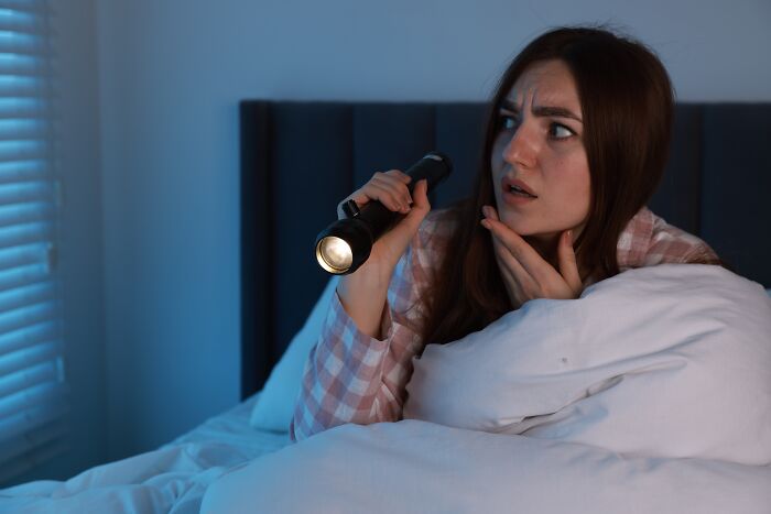 Scared woman in bed holding a flashlight, worried about spooky unexpected noises