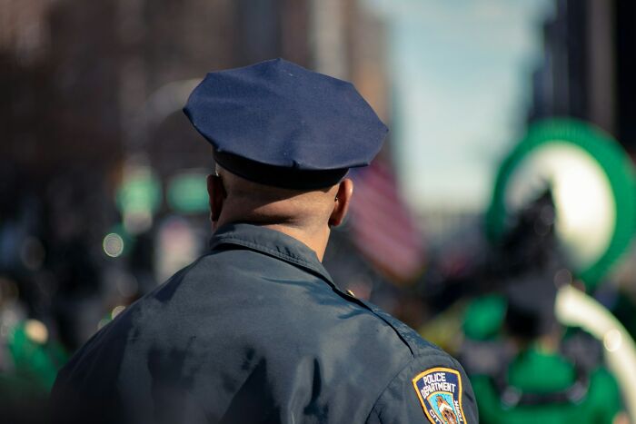 Police officer from behind monitoring a public event wearing uniform and cap