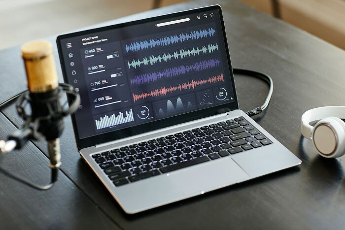 Laptop displaying audio editing software next to microphone and headphones