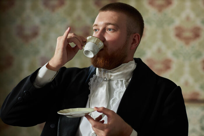 Man in vintage clothing drinking tea from a delicate cup inside a decorated room