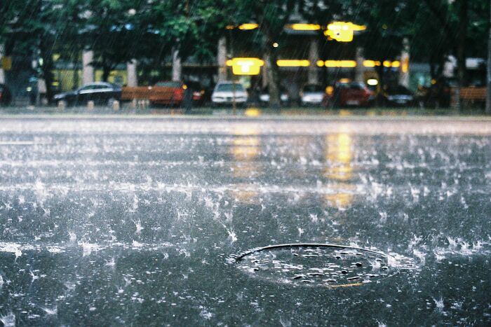 Heavy rain splashing on a city street and manhole cover at night, evoking a scary atmosphere.