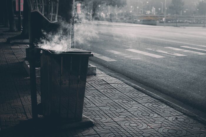 Smoke rising from a public trash can on a deserted street, capturing a weird and creepy event during a night shift.