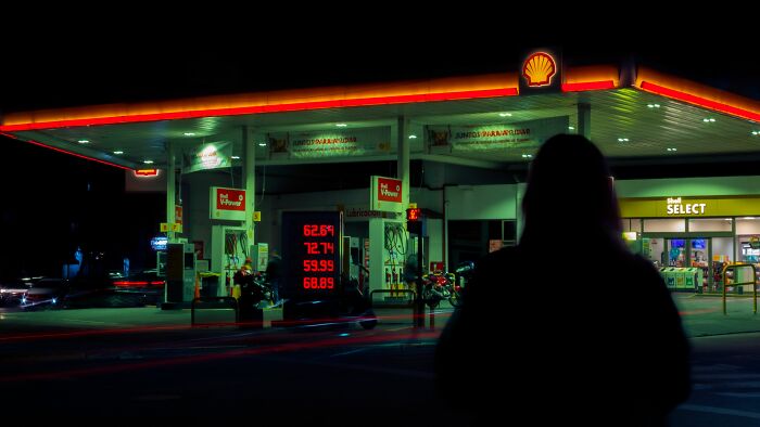 The silhouette of a person looking at a brightly lit gas station at night, suggesting weird things during night work.