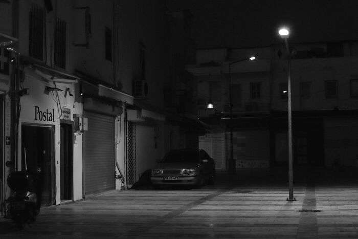 An empty street with a lone car under a street light at night