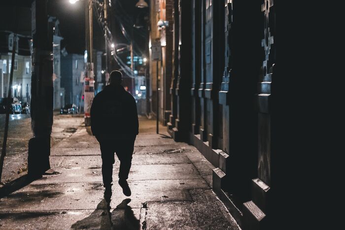 Silhouette of a man walking down a dark city sidewalk at night, suggesting creepy and weird things.