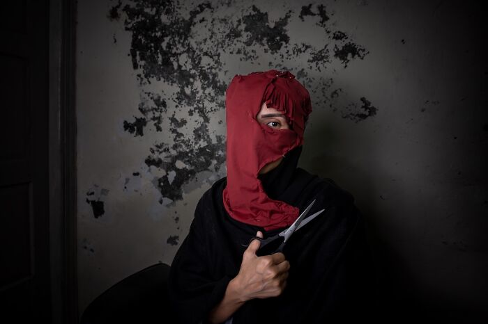 Person with red hood holding scissors in dim room, striking portrait, best pics Siena International Photo Awards 2026