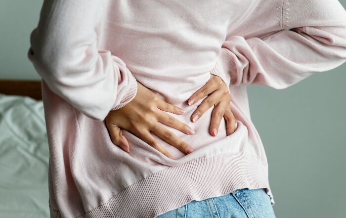 A person holding their painful lower back, representing dumb things professionals said or did to lose trust.