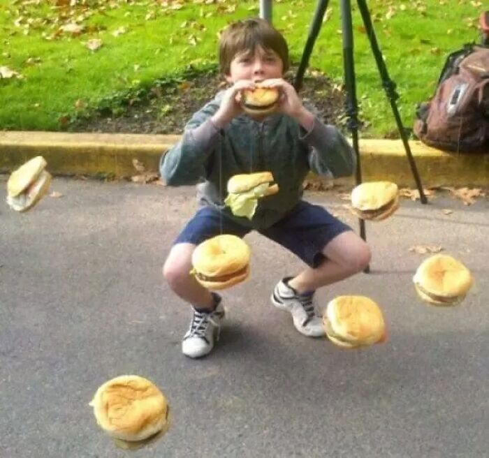Boy squatting outdoors surrounded by floating hamburgers weird cursed image