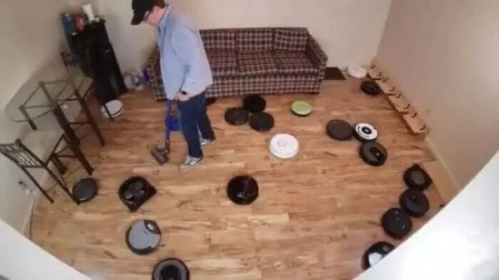 Man vacuuming hardwood floor surrounded by multiple robot vacuum cleaners