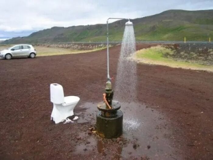 Outdoor shower and toilet set up in open gravel area near road and hills
