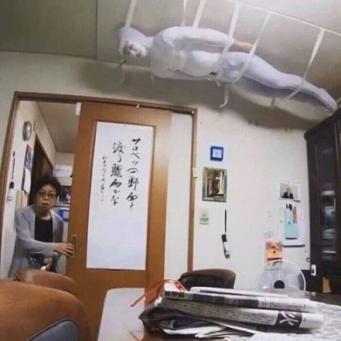 White mannequin strapped to the ceiling of a cluttered room