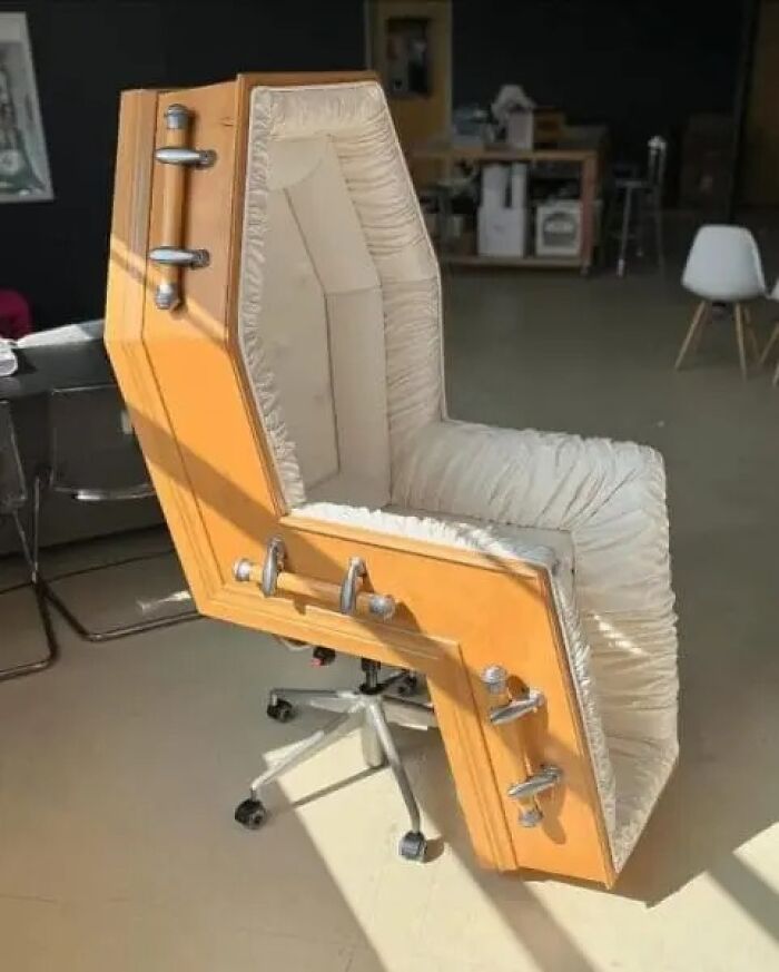 Office chair shaped like a coffin with padded interior and metal handles