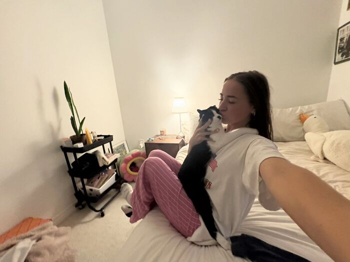 Woman kissing her black and white cat on bed in viral TikTok trend of life stories lived alongside pets