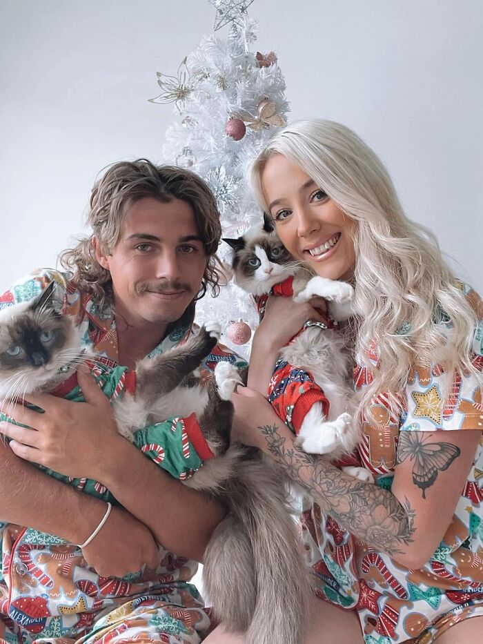 A couple in Christmas pajamas holding their two cats, highlighting a TikTok Trend sharing pet life stories.