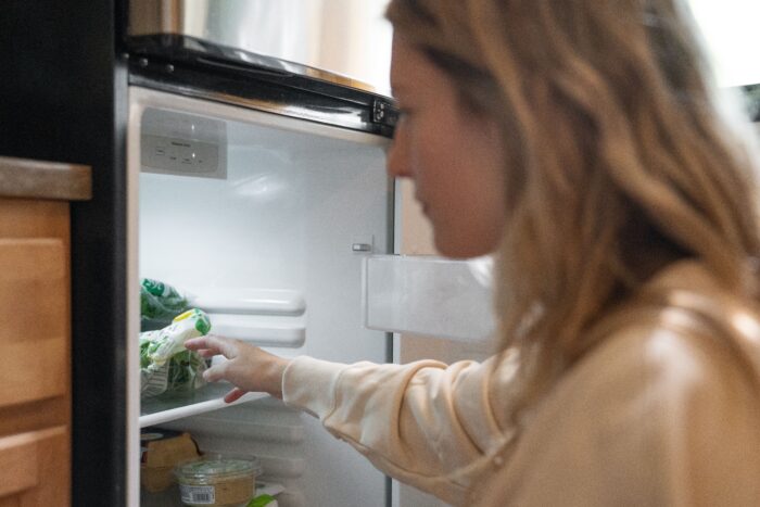 Woman looking inside an open refrigerator for stepchild's food in a home kitchen.
