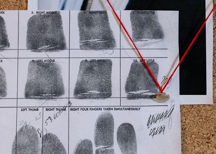 Fingerprint card pinned with red string on an investigation board tied to online mysteries.