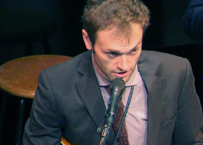 A man speaking into a microphone, tied to strange online mysteries discussed on the internet.
