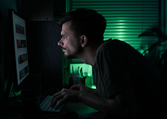 A man staring intensely at a computer monitor in a dark room while researching strange online mysteries.