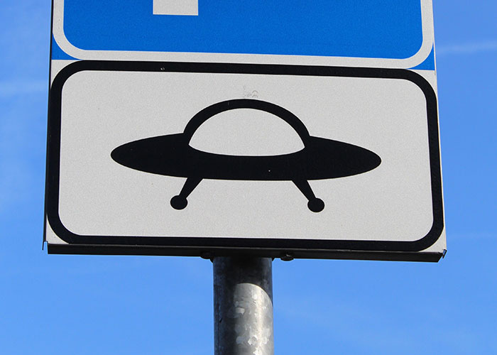 A white road sign featuring a black UFO icon representing online mysteries.