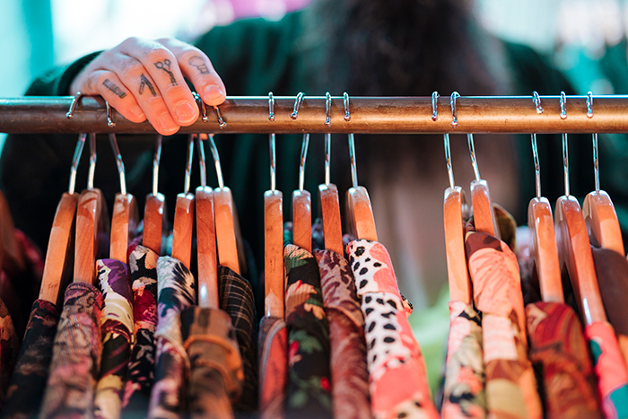 A hand with finger tattoos touching wooden hangers on a clothing rack, focusing on how she dresses. A hand with finger tattoos touching wooden hangers on a clothing rack, focusing on how she dresses.