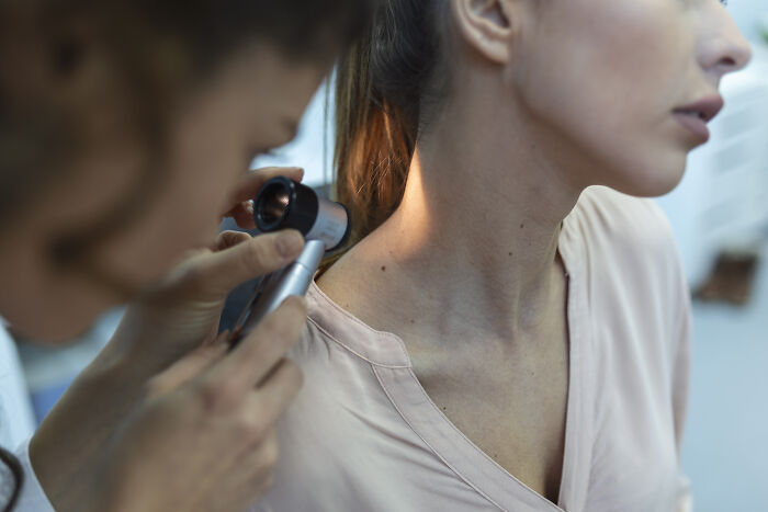 A dermatologist examining a patient's skin with a dermatoscope, showing health problems in Gen Z.