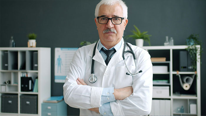A senior male doctor in a white lab coat standing with arms crossed in an office. A senior male doctor in a white lab coat standing with arms crossed in an office.