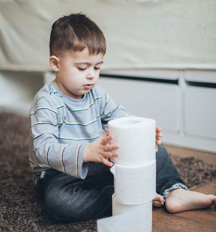 A young child sitting on the floor stacking rolls of toilet paper. A young child sitting on the floor stacking rolls of toilet paper.