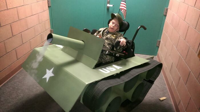 A child in a military costume using an army tank wheelchair cover for a hilarious Halloween outfit idea.