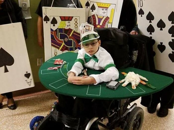 A child in a wheelchair dressed as a poker dealer with giant playing card costumes